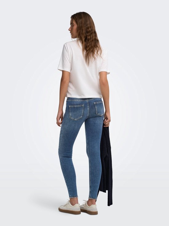 Vrouw in blauwe skinny jeans met lichte wassing, rafelige zoom en witte top.