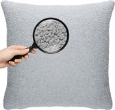 Een lichtgrijs teddy kussen met een vergrootglas dat de textuur laat zien. Een hand houdt het vergrootglas vast.