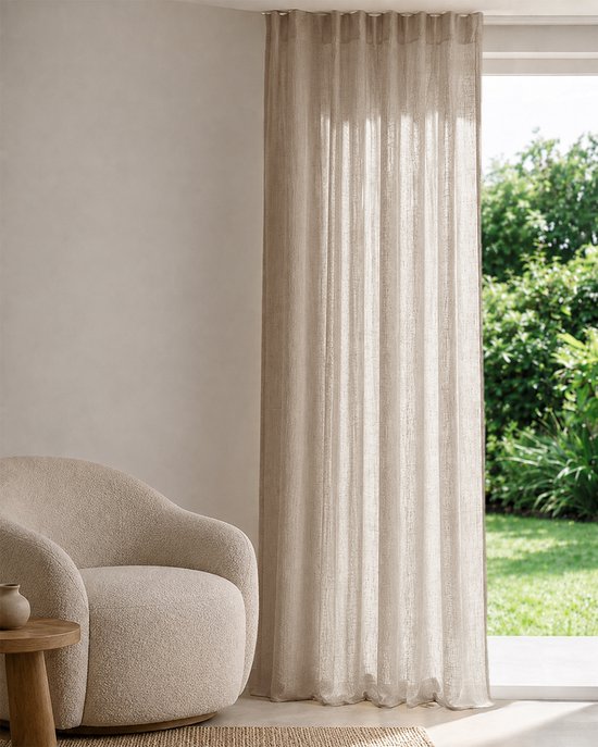 Rideau inbetween beige clair dans un salon avec un fauteuil couleur sable. Vue sur jardin verdoyant à travers la fenêtre.