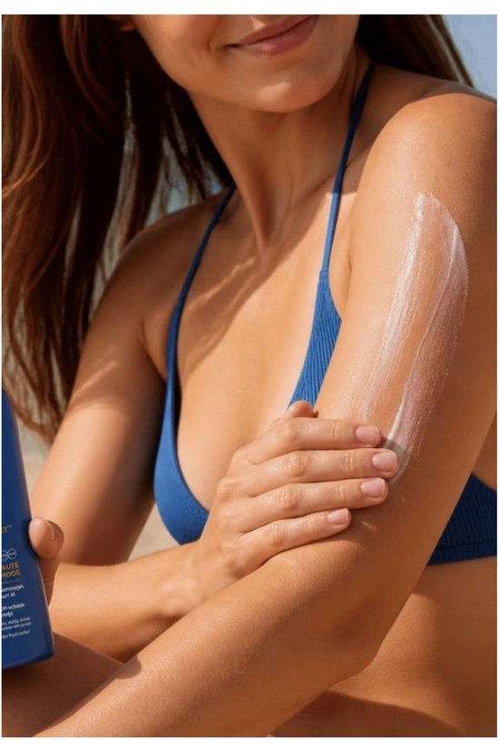 Een vrouw in een blauw bikinibroekje brengt zonnebrandcrème aan op haar arm.