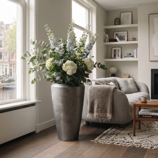 Grand vase métallique gris argenté avec un bouquet touffu de fleurs blanches et bleu clair et de verdure.
