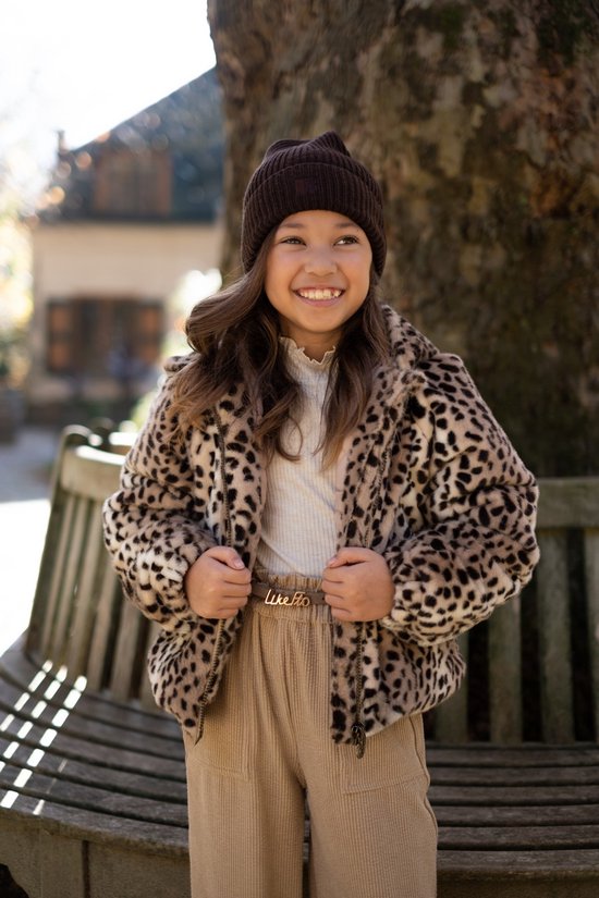 Meisje met bruine muts draagt bruin-zwarte luipaardprint jas, beige coltrui en beige broek.