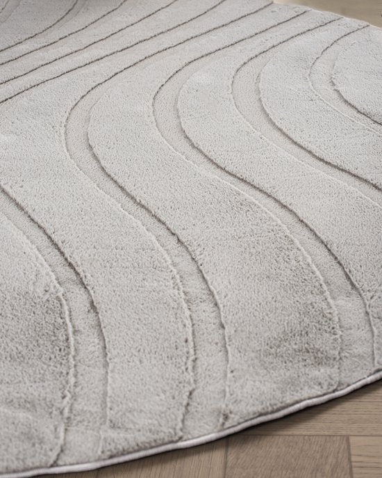Gros plan d'un tapis rond taupe avec un motif de lignes ondulées en relief.