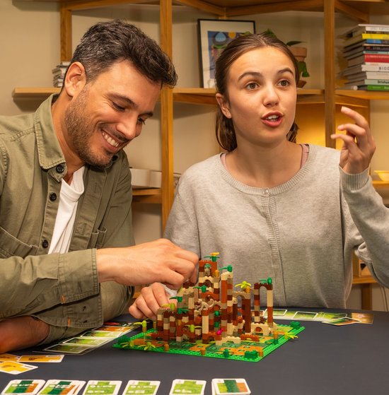 Een vader en dochter spelen LEGO Monkey Palace met een bruine, oranje en beige toren.