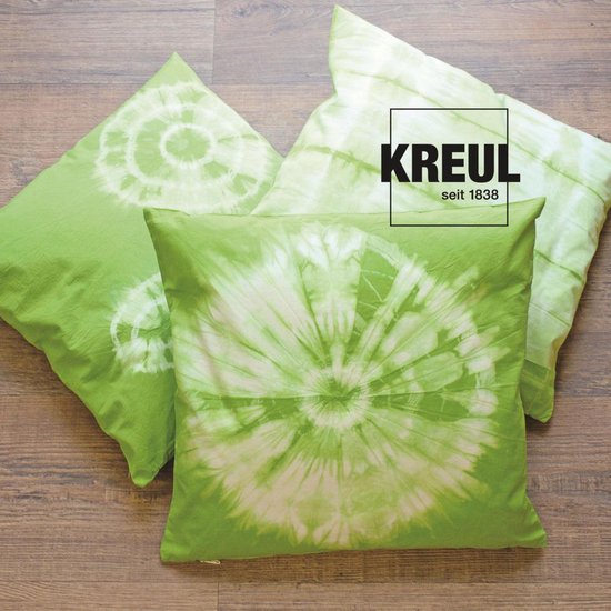 Trois coussins verts avec un imprimé batik blanc en spirale sur un fond en bois.