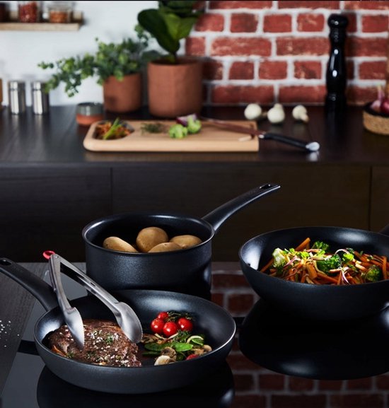 Een kookpan met aardappelen, een koekenpan met een steak en tomaatjes, en een wokpan met groenten.