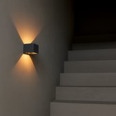 Zwarte wandlamp die warm licht schijnt, naast donkere trap