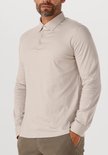 Man met handen in de zakken, draagt een beige longsleeve poloshirt.