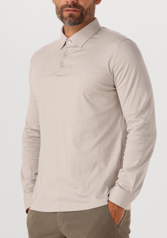 Man met handen in de zakken, draagt een beige longsleeve poloshirt.