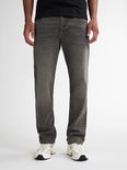 Man in een zwarte T-shirt en grijze jeans, staand.