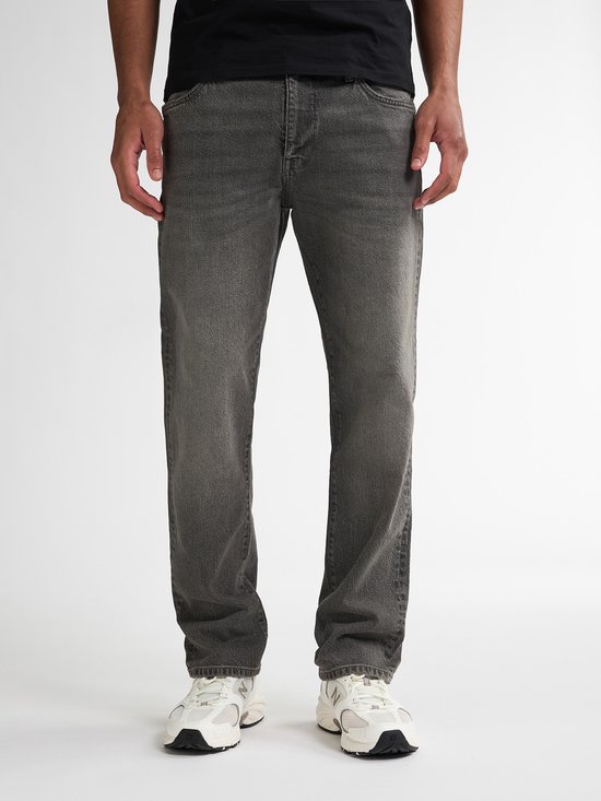 Man in een zwarte T-shirt en grijze jeans, staand.