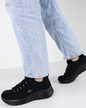 Een persoon draagt zwarte Skechers Arch Fit sneakers met een lichtblauwe jeans.