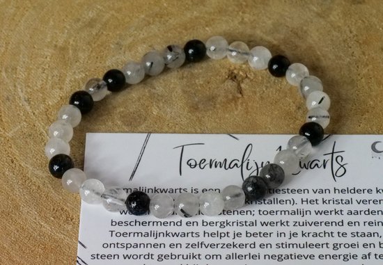 Armband van heldere kwarts en zwarte toermalijn kralen op een houten ondergrond.