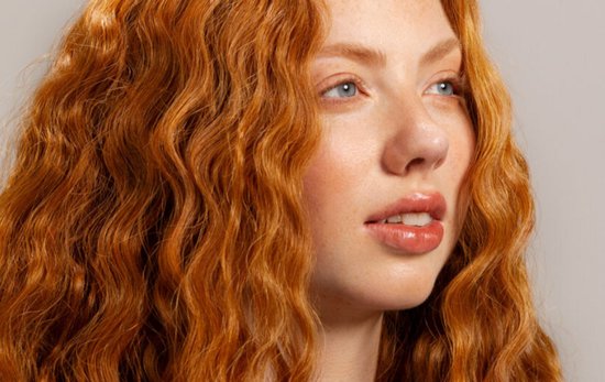 Close-up van een vrouw met lang, golvend, rood haar en sproeten.