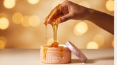 Hand schenkt dikke gouden honing uit een potje 'Wondr Hair Mask'.