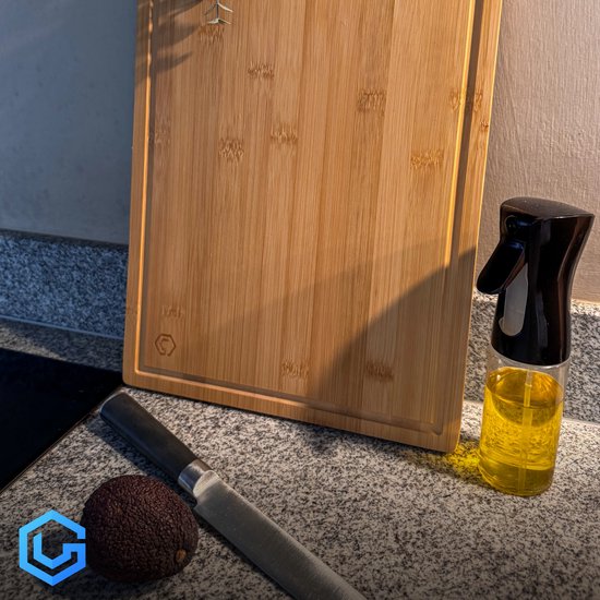 Bamboe snijplank met een geul, naast een avocade, mes en oliespray.