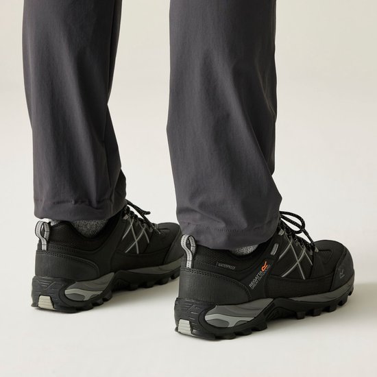 Achterkant van zwarte wandelschoenen met grijze details, gedragen door een persoon in een grijze broek.