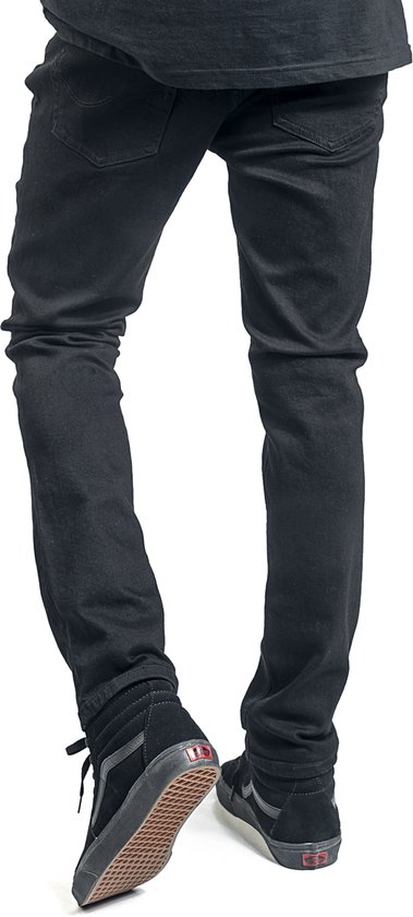 Achterkant van de benen van een man in zwarte skinny jeans en zwarte hoge Vans sneakers.
