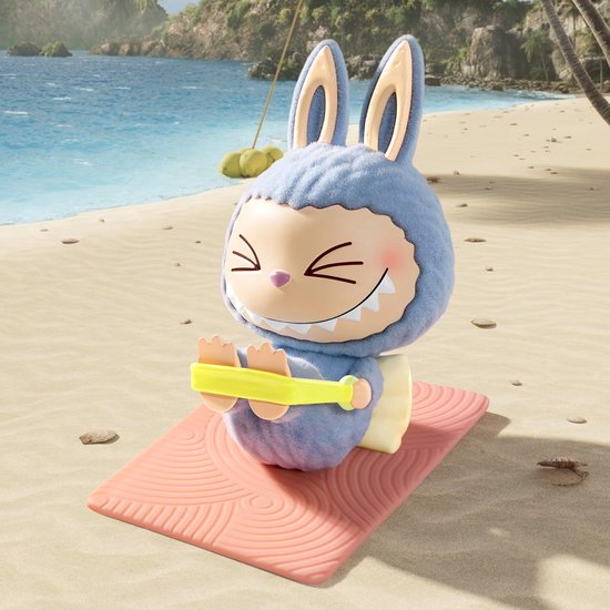 Blauwe harige pop met gesloten ogen, zittend op een roze yogamat op een strand.