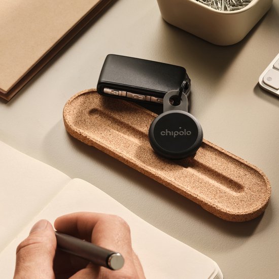 Chipolo tracker op een bureau naast een sleutelbos en notitieboek.