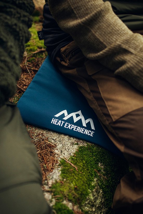 Blauw verwarmd kussen met "HEAT EXPERIENCE" logo, op mos en stenen, in de natuur.