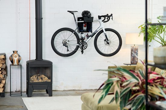Witte racefiets met een Stasdock muurbeugel, opgehangen aan een witte bakstenen muur.
