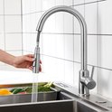 Zilverkleurige keukenkraan met uittrekbare sproeier die water spuit in een gootsteen.