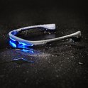Grijze lichttherapiebril met blauw licht, liggend op een natte, donkere ondergrond.