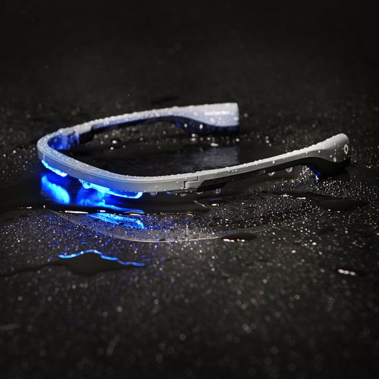 Grijze lichttherapiebril met blauw licht, liggend op een natte, donkere ondergrond.