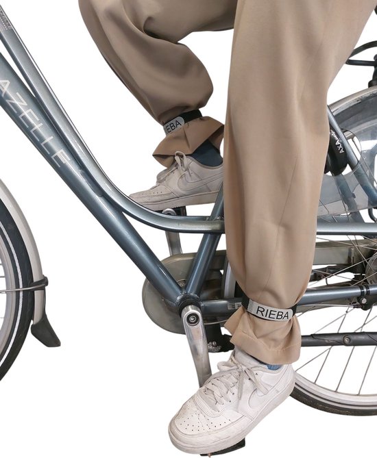 Persoon op een fiets, met beige broekspijpen die omhoog zijn gerold en zwarte broekklemmen met reflecterend 'RIEBA' logo.