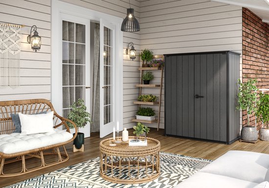 Abri de jardin gris à double porte, à côté d'un banc en rotin et d'une table basse ronde sur une terrasse.