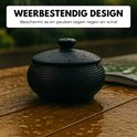 Zwarte, geribbelde keramische asbak met deksel op een natte houten tafel in de regen.