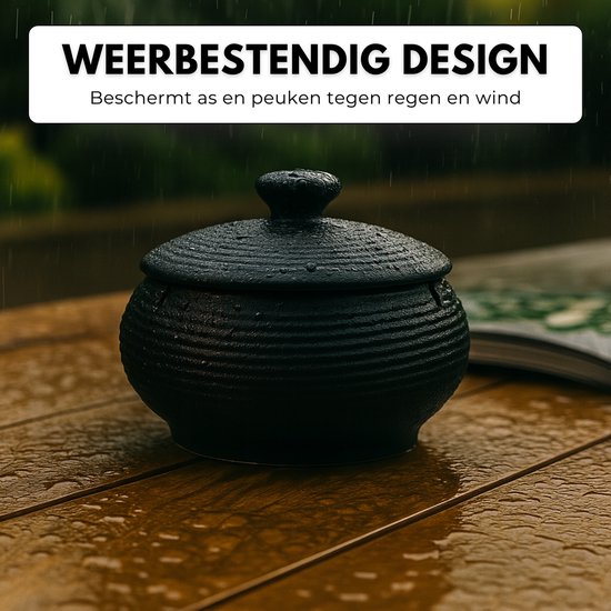 Zwarte, geribbelde keramische asbak met deksel op een natte houten tafel in de regen.