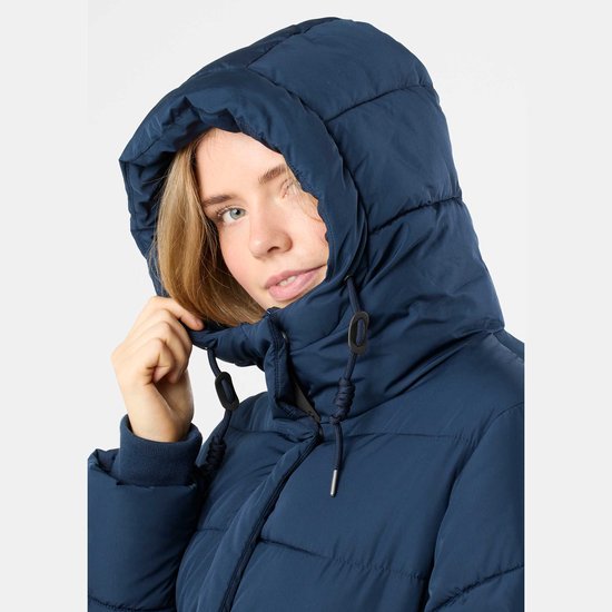 Jonge vrouw met een donkerblauwe, gewatteerde winterjas met capuchon. Ze trekt de capuchon dichterbij.