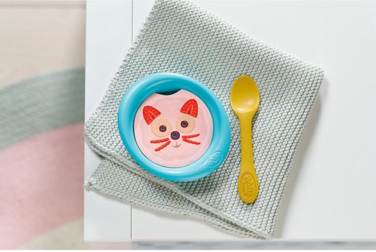 Blauw kommetje met kattengezicht, aardbeien en een gele lepel erop.