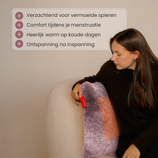 Une femme se détend sur un canapé, tenant un coussin chauffant rose et doux sur ses genoux.