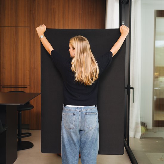 Vrouw met blonde haren in zwart shirt en spijkerbroek houdt de Puzzlup puzzelmat omhoog.