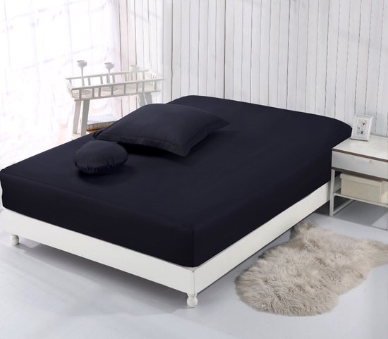 Zwart hoeslaken op een wit bed met een donkergrijs kussen en een rond kussen.