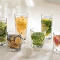 Un groupe de verres remplis de diverses boissons fruitées comme du kiwi, de l'orange, de la menthe, des myrtilles et du pamplemousse, posés sur de la glace.