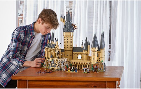 Jongen kijkt naar een grote LEGO Harry Potter Zweinstein Kasteel set met minifiguren.