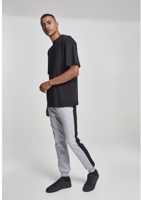 Man met korte haren, draagt een zwart T-shirt en grijze joggingbroek met zijstreep.