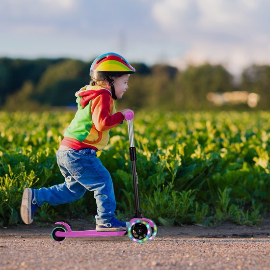 Kind met helm rijdt op een roze step met lichtgevende wielen in een groen veld.