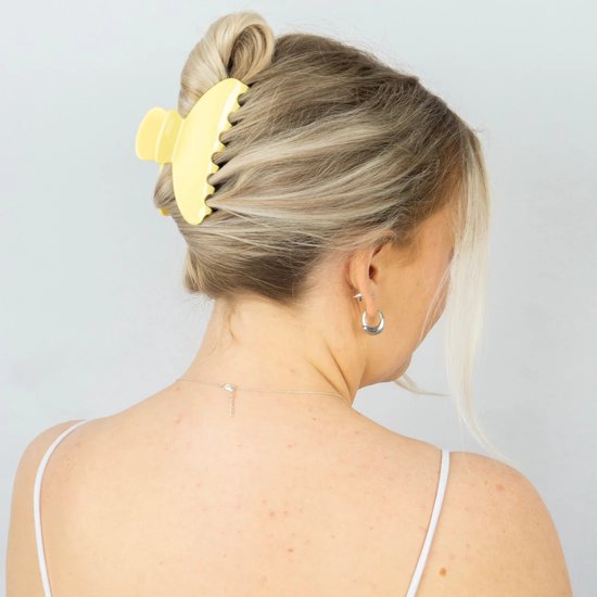 Blonde vrouw met een gele haarklem in opgestoken haar, gezien vanaf de achterkant.