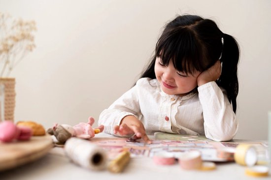 Meisje met staartjes speelt met een stickerboek en stoffen pop op tafel.