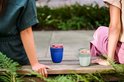 Twee vrouwen zitten buiten op een houten bank met elk een yoghurtbeker voor zich.