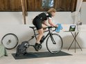 Vrouw traint binnen op Tacx trainer op zwarte mat, bij laptop.