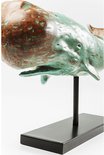 Detail van een verweerd turquoise en bruin houten walvisbeeld, met open mond, op een zwarte standaard.