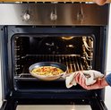 Een hand haalt een koekenpan met omelet uit een open oven.