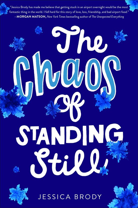 Boekcover met de titel 'The Chaos of Standing Still' in blauwe en witte letters op een donkerblauwe achtergrond, met abstracte blauwe bloemblaadjes.