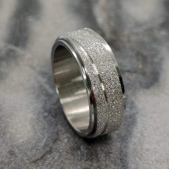Zilverkleurige ring met een glinsterende, gestreepte band, op een marmeren achtergrond.